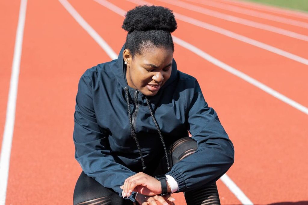 Vrouw met donkere kleding is hartslagzones aan het berekenen tijdens hardlopen op een atletiekbaan