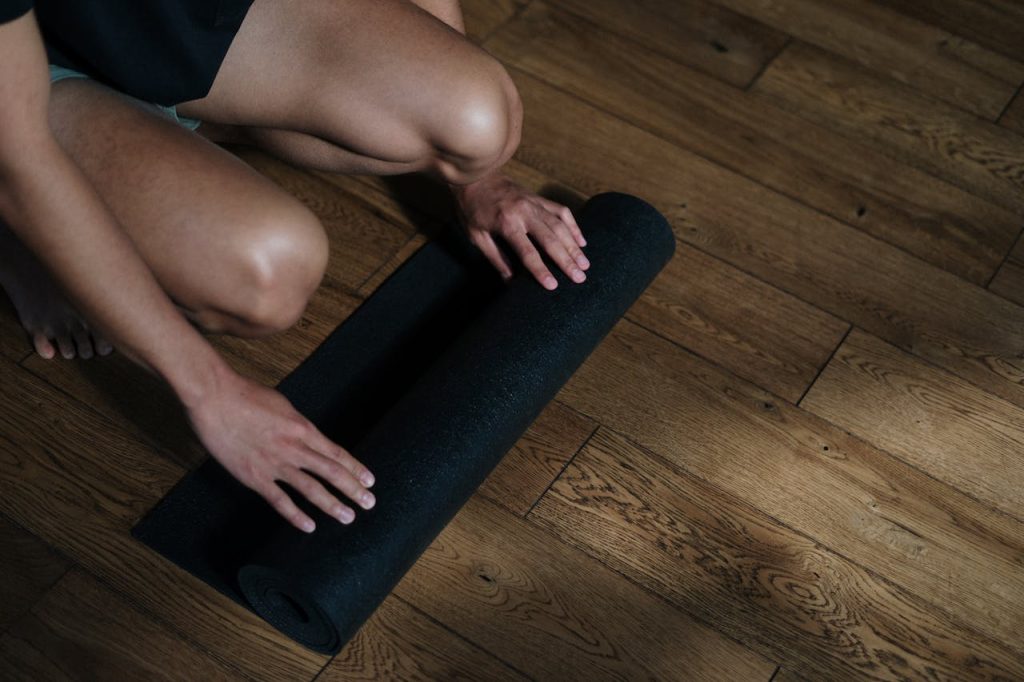 persoon doet yoga met een matje op een houten vloer