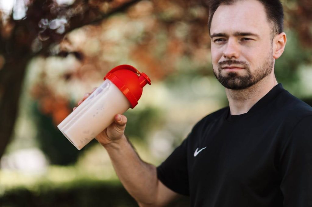 Man met zwart shirt drinkt uit plastic shakebeker met rode dop