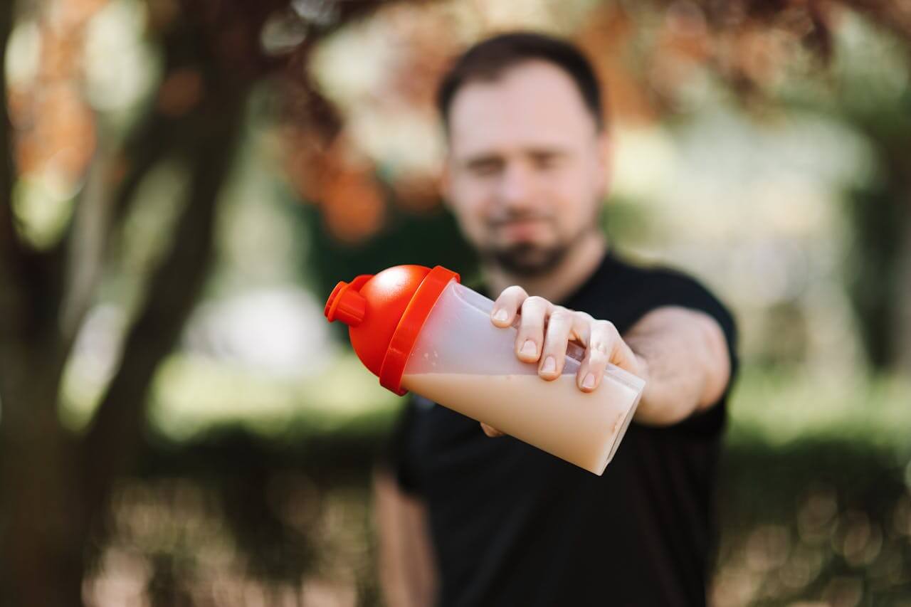 Man houdt plastic shakebeker met rode dop vast