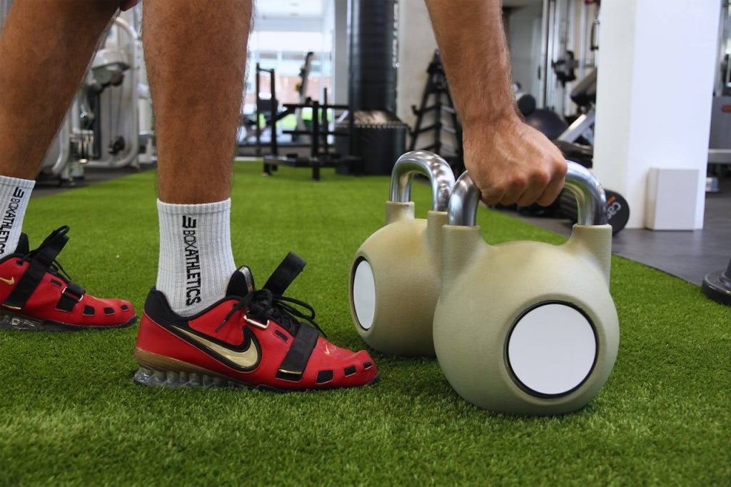 Man met rode schoenen tilt kettlebell op in de sportschool