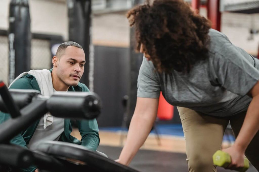 Mannelijke personal trainer is vrouwelijke client in grijs shirt aan het motiveren tijdens haar training